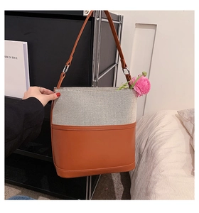 Detail of canvas and brown leather bucket bag with metallic ring and crossbody strap