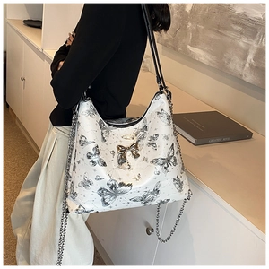 Close-up of white butterfly print tote bag with gold metal charm and chain strap