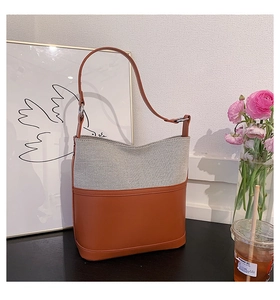 Detail view of a half-moon tote bag featuring grey canvas and brown leather patchwork