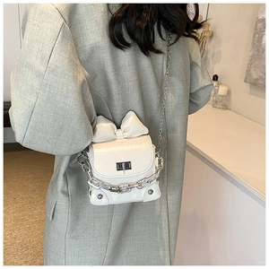 Detail of white bow crossbody bag with silver chains and crocodile texture on a model