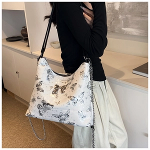 Detail of white tote bag with silver butterfly prints and metal chain strap on model