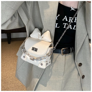 Detail of a creamy white mini box bag featuring a large bow and elegant silver chain strap