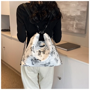 Detailed view of white tote bag featuring black butterfly prints and silver chain strap