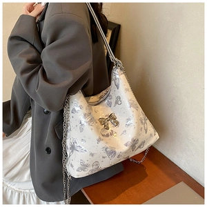 Detail of white butterfly tote bag with metal bow accent and silver chain strap
