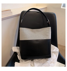 Detail of contrast canvas bucket bag with black leather trim on a leather chair