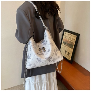 Shoulder bag detail showing silver butterfly print and metal chain strap on model