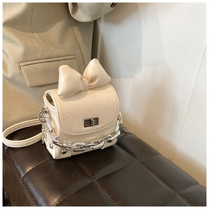 Detail of a mini cream bow box bag with a silver chain and textured synthetic leather