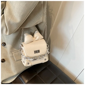 Close-up of cream mini bow bag with silver chain strap and metal turn-lock on suit