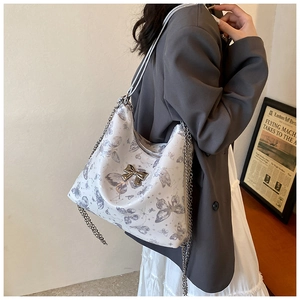 Close-up of white butterfly print tote bag with silver metallic bow and chain strap