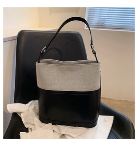Detail of canvas and black leather bucket bag on a leather chair with soft natural light