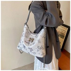 Detail of white tote bag featuring grey butterfly patterns and metal bow hardware