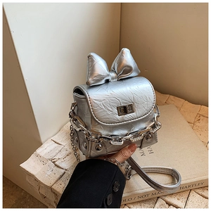 Detail showing mini silver bow bag with crinkled metallic texture and chain strap