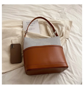Detail view of brown leather and grey tweed bucket bag on white fabric background