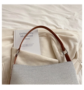 Close-up of beige canvas bucket bag with brown leather handle on a soft knit blanket