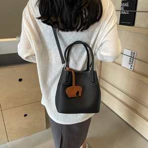 Black lychee leather bucket bag with orange elephant charm shown on a model