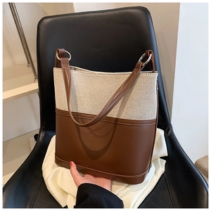 Detail of a color-block bucket bag showing canvas and brown leather texture with metal ring