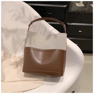 Detail of a brown leather and beige canvas bucket bag with adjustable shoulder strap