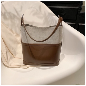 Detail of color-block bucket bag showing brown leather trim and canvas texture on a chair