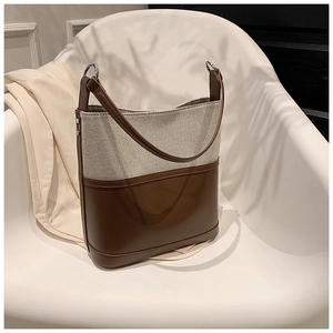 Detail of a chic bucket bag with beige canvas and brown leather stitching on a chair