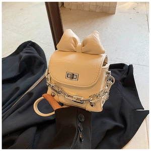 Detail of a creamy white mini box bag with oversized bow and silver chain strap