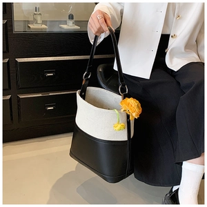Chic two-tone canvas bucket bag with black leather trim worn by a model in a minimalist setting