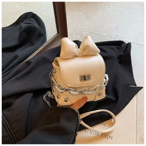 Detail of cream mini box bag with oversized bow and elegant metal chain on black blazer