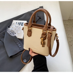 Détail du sac seau bicolore avec texture cuir raffinée et pendentif ours en métal