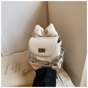 Detail of cream white pleated crossbody bag featuring a large bow and silver chain strap