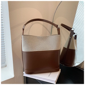 Detail of contrast bucket bag showing brown leather trim and beige canvas texture