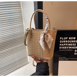 Close-up of beige woven bucket bag with floral silk scarf detail and adjustable strap