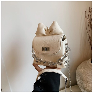 Detail of cream mini bow bag with silver twist lock and decorative chain on black coat