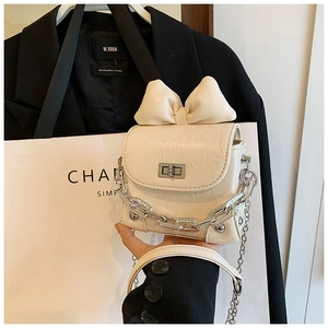 Detail of a mini cream-colored box bag with a large bow and silver chain strap