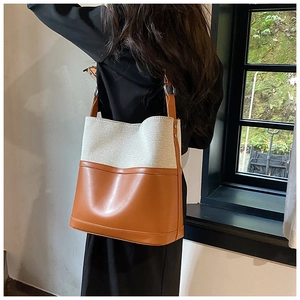 Detail of canvas and brown leather bucket bag with metal rings shown on shoulder