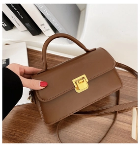 Dettaglio di borsa marrone con fibbia quadrata dorata minimalista e tracolla sottile