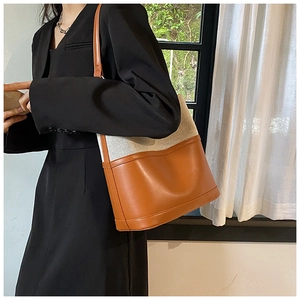 Detail of canvas and brown leather stitching on a tote bag worn by a model