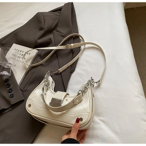 Detail of cream quilted hobo bag with silver chain and metal clasp on brown fabric