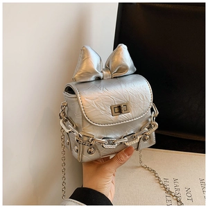 Detailed close-up of the silver mini box bag with metallic bow and chain strap