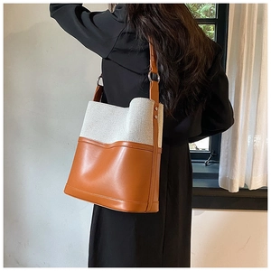 Detail of two-tone bucket bag featuring brown leather and off-white canvas texture