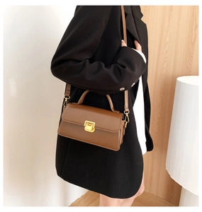 Dettaglio di una borsa a tracolla vintage marrone con chiusura dorata su un cappotto nero