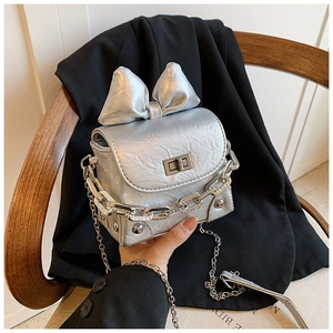 Detail of silver metallic mini bag featuring a large bow and decorative chain strap