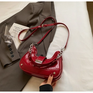 Detail of burgundy crescent bag featuring glossy cracked leather and silver metal hardware