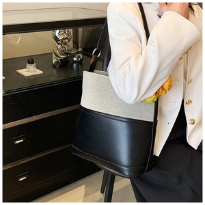 Detail of canvas and black leather bucket bag shown on a model in a modern studio