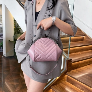 Pink quilted shell bag with metallic ring handle and chain strap on a wooden staircase