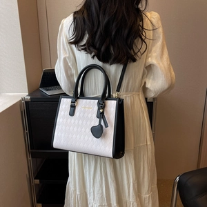Quilted tote bag with black contrast straps and heart charm on a minimalist background