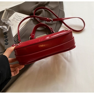 Detailed side view of glossy red handbag showing silver studs and reinforced bottom
