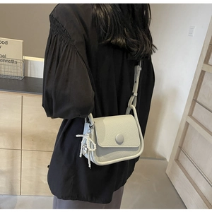 Detail of light grey lychee pattern leather saddle bag with beaded bow pendant