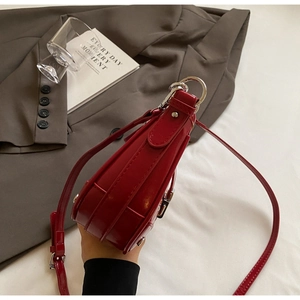 Side view of a red patent leather saddle bag with silver hardware and a sleek finish