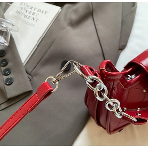 Detailed macro shot of red patent leather bag with silver chain strap and metal lobster clasp