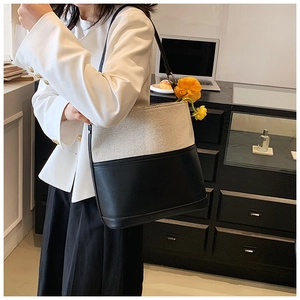 Detail of minimalist two-tone canvas and black leather tote bag worn with casual office wear