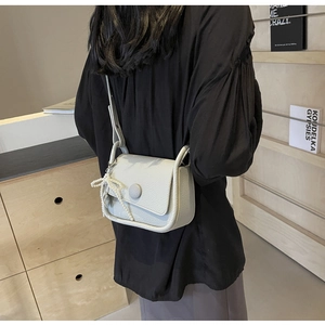 Detail of light gray litchi texture leather saddle bag with pearl bow charm